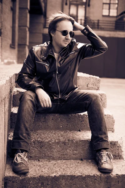 Jonge man in zonnebril en een leren jas zittend op stenen trap — Stockfoto