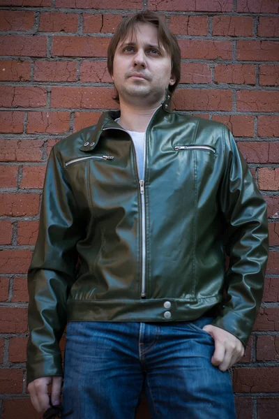 De jonge man in een lederen jas staande in de buurt van een muur — Stockfoto