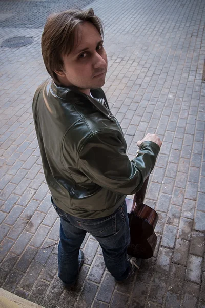 De jonge man in een lederen jas met een gitaar — Stockfoto