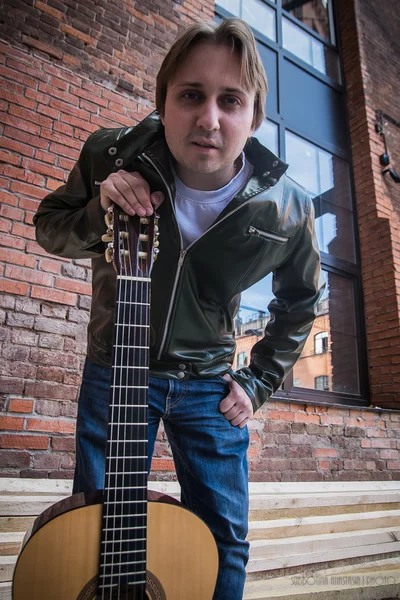 De jonge man in een lederen jas met een gitaar — Stockfoto