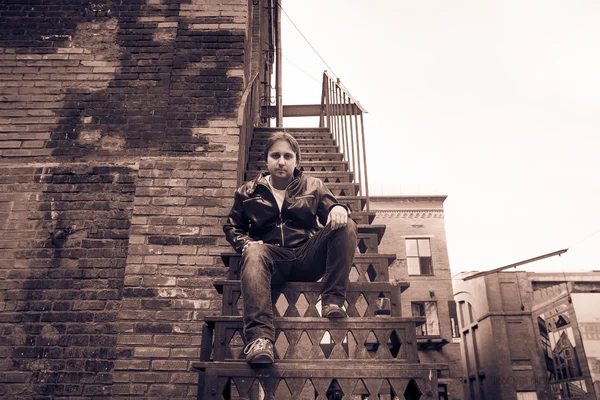 The young man in a leather jacket sitting on an iron ladder — Stock Image The young man in a leather jacket sitting on an iron ladder Royalty Free Stock Photos