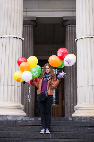 Mujer joven con globos de colores de pie en las escaleras adornadas con columnas —  Fotos de Stock
