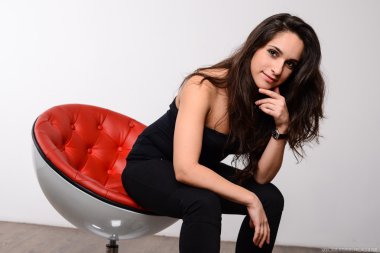 Siyah elbiseli kırmızı bir sandalyede oturan uzun siyah saçlı genç kız