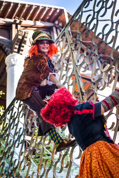 Mujer joven y hombre en la imagen del Sombrerero y la Reina Roja del cuento de hadas sobre Alice subir a la valla — Foto de Stock