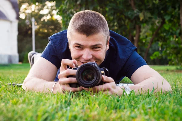 Den unge mannen med kameran ligga på gräset och leende — Stockfoto