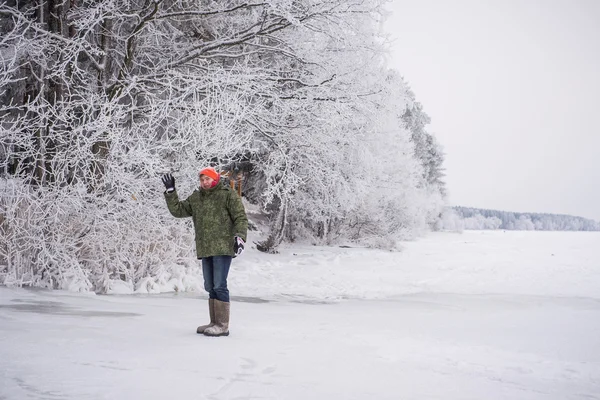 A young man in warm clothes standing near the forest on the banks of the river — Stock Photo, Image