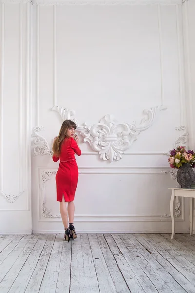 Young slim girl posing in a bright red dress in a historic interior with stucco — Stock Photo, Image