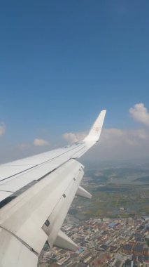 VERTICAL FOOTAGE, mavi gökyüzü ve yolcu uçağının lombozu dışında beyaz bulutlar, uçağın kanadı, yerde yüksek binalar var