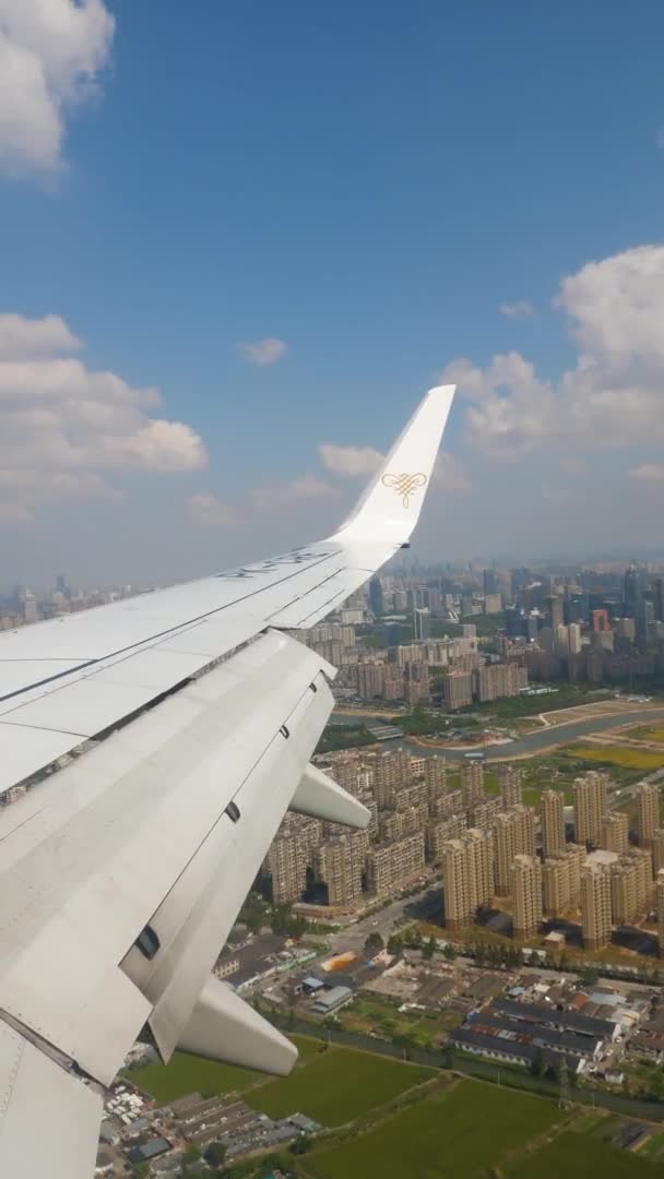 VERTICAL FOOTAGE, пасажирський літак збирається приземлитися на малій висоті, крила порту виходять з блакитного неба і білих хмар, і є високі будівлі на землі — стокове відео