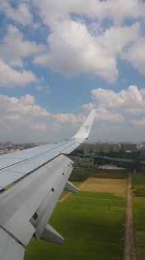 VERTICAL FOOTAGE, mavi gökyüzü ve yolcu uçağının lombozu dışında beyaz bulutlar, uçağın kanadı, yerde yüksek binalar var