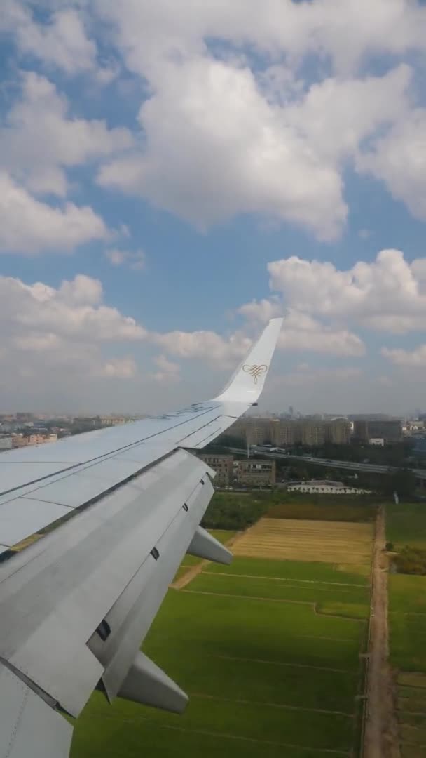 VERTICAL FOOTAGE, блакитне небо і білі хмари за межами отвору пасажирського літака, крило літака, є високі будівлі на землі — стокове відео