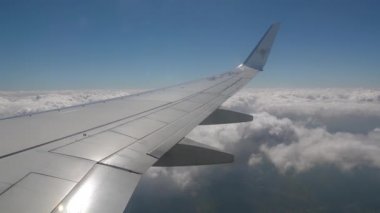 Sivil bir uçakla seyahat ederken, pencerenin dışındaki kanat gökyüzünde, mavi gökyüzü ve beyaz bulutlar 10.000 metre yükseklikte.