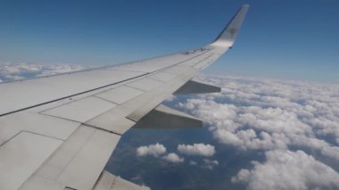 Sivil bir uçakla seyahat ederken, pencerenin dışındaki kanat gökyüzünde, mavi gökyüzü ve beyaz bulutlar 10.000 metre yükseklikte.