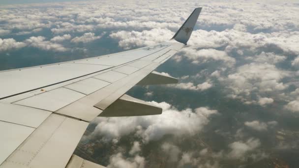 Путешествуя на гражданском самолете, крыло за пределами иллюминатора находится в небе с голубым небом и белыми облаками на высоте 10 000 метров — стоковое видео