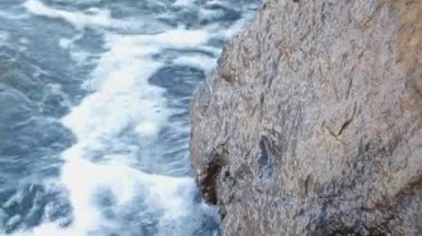Dalgalar kıyıdaki kayaların üzerinden geçti. Mavi berrak su yüzeyi