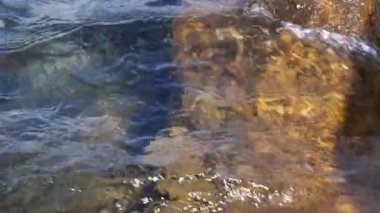 Dalgalar kıyıdaki kayaların üzerinden geçti. Mavi berrak su yüzeyi