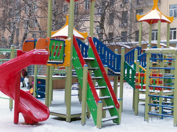 Empty playground in a yard, covered with snow, focus in the background