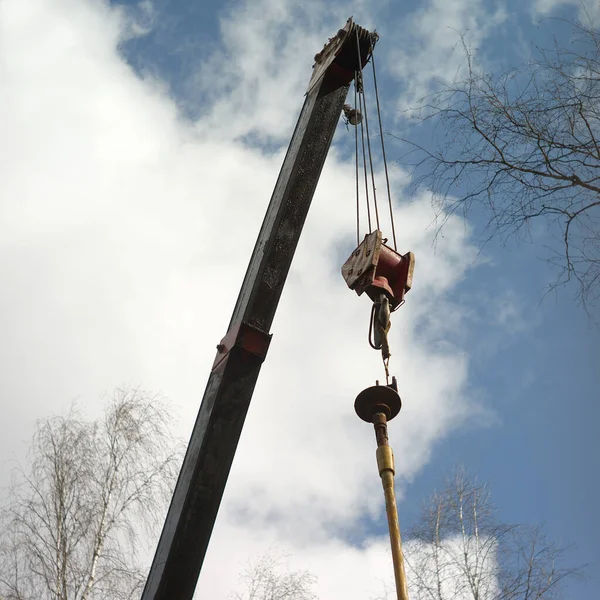 A crane arm lifting a pipe, outdoor shot against the sky