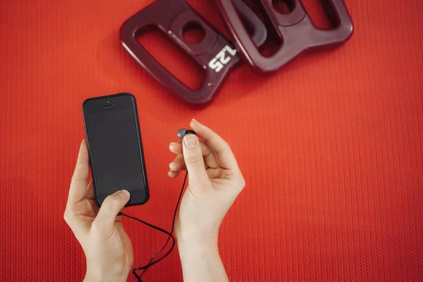 Young woman resting after workout. Healthy young female taking break after training in gym with phone in hands over a red fitness carpet. — Stock Photo, Image