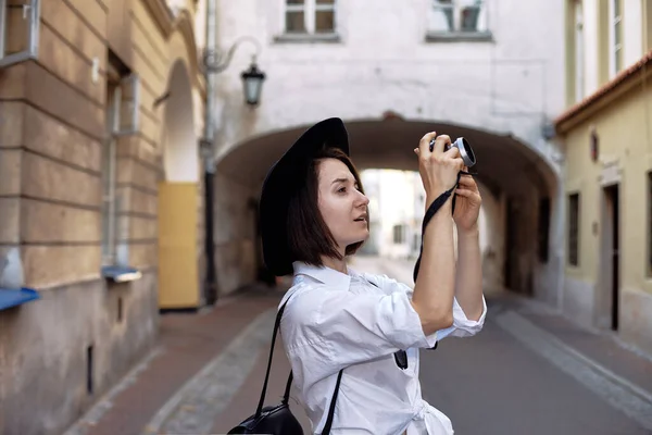 若い女の子写真家 その少女は黒い髪をしている 彼女は黒い帽子とサングラスをかけていて カメラは古いヨーロッパの街の道路に立っています — ストック写真