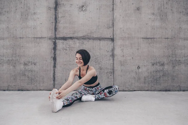Kız dışarıda çalışıyor. Yerde oturarak esniyor. Arkaplan olarak beton duvar