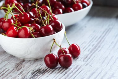 Beyaz bir kasede beyaz ahşap masada kirazlar.