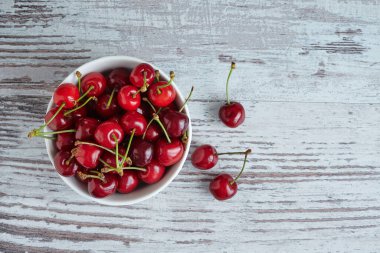 Beyaz bir kasede beyaz ahşap masada kirazlar.