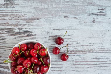 Beyaz bir kasede beyaz ahşap masada kirazlar.