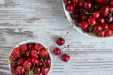 Beyaz bir kasede beyaz ahşap masada kirazlar.
