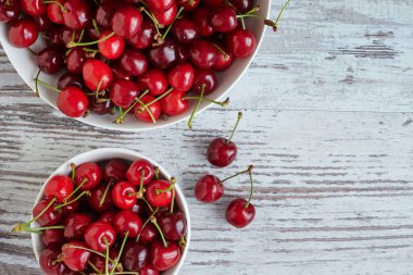 Beyaz bir kasede beyaz ahşap masada kirazlar.