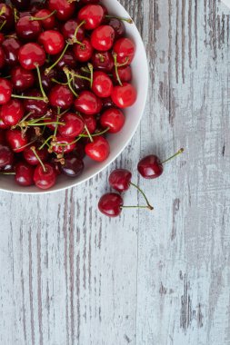 Beyaz bir kasede beyaz ahşap masada kirazlar.