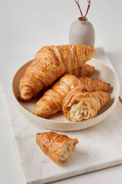 Beyaz tabakta kruvasanlar. Tabak mermer bir tahtanın üzerinde. Arka planda bir vazo