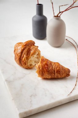 Beyaz tabakta kruvasanlar. Tabak mermer bir tahtanın üzerinde. Arka planda iki vazo var.