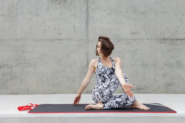 Fitness girl in black and white fitness suite outdoor workout. Against a gray concrete wall.