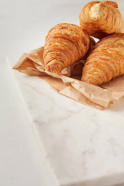 Croissants en el papel pergamino, en el tablero de marbel — Foto de Stock