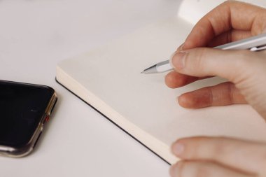 Bir erkek çalışıyor. Not alıyorum. Akıllı telefon masanın üstünde.