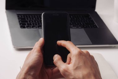 Erkek, elinde siyah bir akıllı telefon ve not defterine yazı yazıyor..