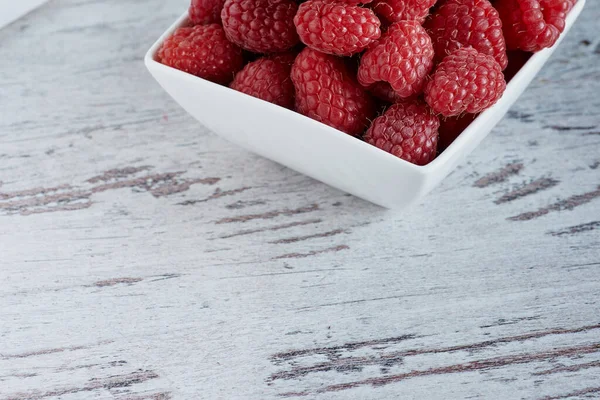 Beyaz ahşap bir masada beyaz bir kasede ahududu fotoğrafı..