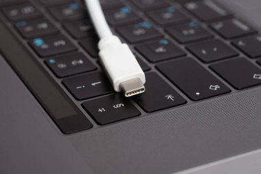Dizüstü bilgisayarın klavyesinde duran beyaz tip c kablosunun yakın plan fotoğrafı.