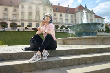 Avrupa bahçesinde merdivenlerde oturan genç bir bayan gezgin. Yaz seyahati