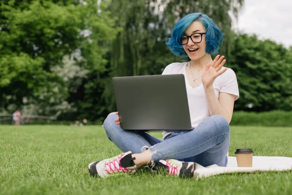Mavi saçlı genç kadınlar ellerinde dizüstü bilgisayarlarıyla yeşil çimlerde oturuyorlar. Yaz zamanı.