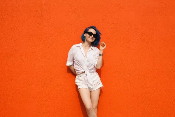 Turuncu arka planda yalnız duran sevimli genç bir bayan resmi. Kameraya bak.