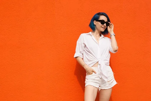 Turuncu arka planda yalnız duran sevimli genç bir bayan resmi. Kameraya bak.