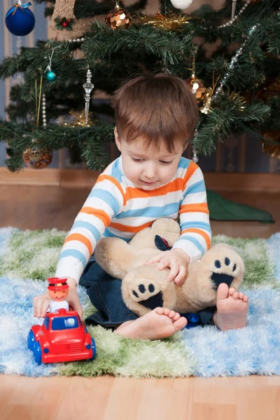 Liten pojke med en nallebjörn och en maskin på julgranen — Stockfoto