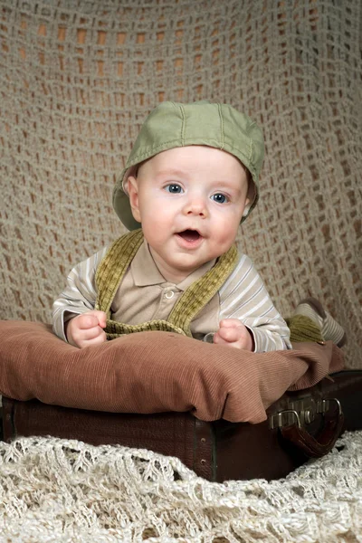 Bebé sonriente (3,5 meses) en una gorra acostado en la maleta retro Imágenes de stock libres de derechos