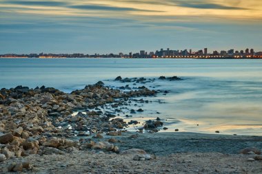 Gün batımında sıcak renklerden oluşan plajın ardında bir şehir var.