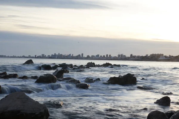 Gün batımında sıcak renklerden oluşan plajın ardında bir şehir var.