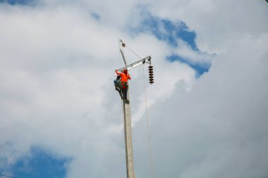 Mavi gökyüzü arka planına sahip elektrik direğinde inşaat işçisi.