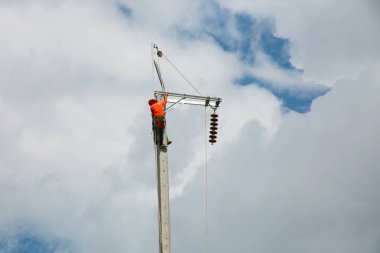 Mavi gökyüzü arka planına sahip elektrik direğinde inşaat işçisi.