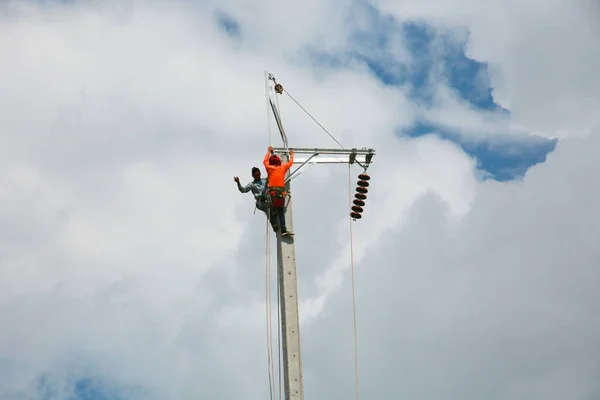 Mavi gökyüzü arka planına sahip elektrik direğinde inşaat işçisi.